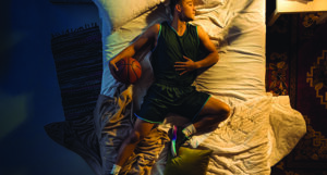 image shows a male athlete sleeping on a bed with a basketball