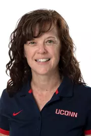 image shows patti kula headshot; woman wearing navy blue UConn polo with brown curly hair