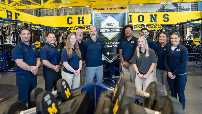 image shows a group of strength coaches posing with an award banner in a weight room